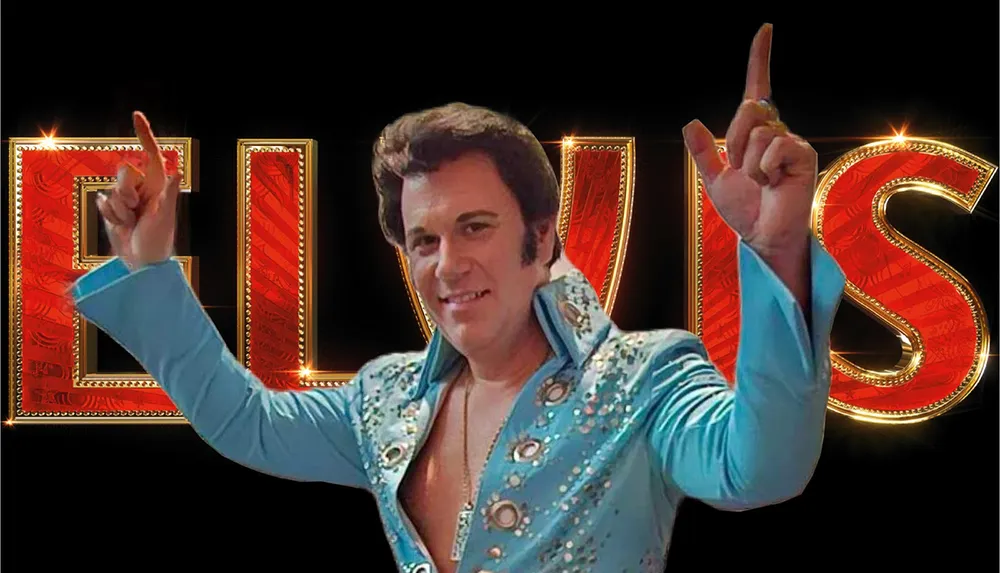 The image depicts a man in a bejeweled blue jumpsuit with his arms raised and the name ELVIS prominently displayed in large decorative letters in the background