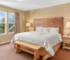This image features a neatly arranged bedroom with a large bed wooden furniture and a window with a view of greenery and distant mountains