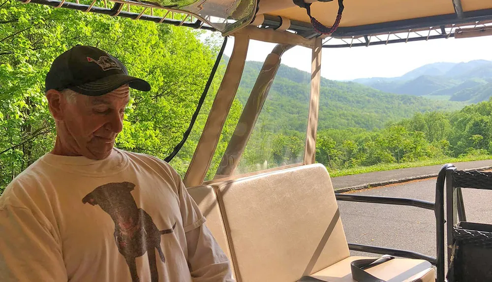 A person is sitting in a golf cart with a scenic view of green rolling hills in the background