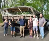 Five people are posing for a photo in front of a rugged safari-style vehicle outdoors on a sunny day