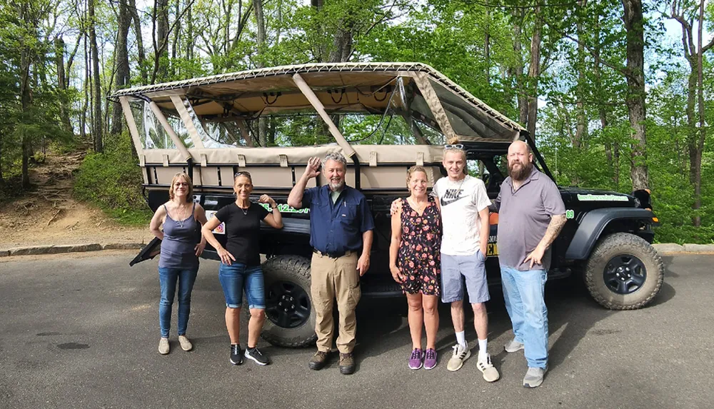 Five people are posing for a photo in front of a rugged safari-style vehicle outdoors on a sunny day