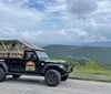 A modified off-road vehicle is parked on a scenic overlook with expansive views of rolling hills and cloudy skies