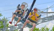 A child and an adult are enjoying a ride on a suspended roller coaster with the adult holding a microphone.