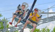 A child and an adult are enjoying a ride on a suspended roller coaster with the adult holding a microphone.