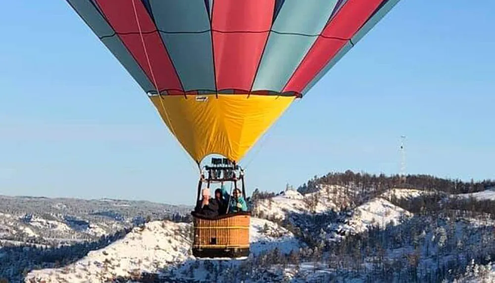 A colorful hot air balloon floats above a snowy landscape with passengers inside the basket enjoying the view