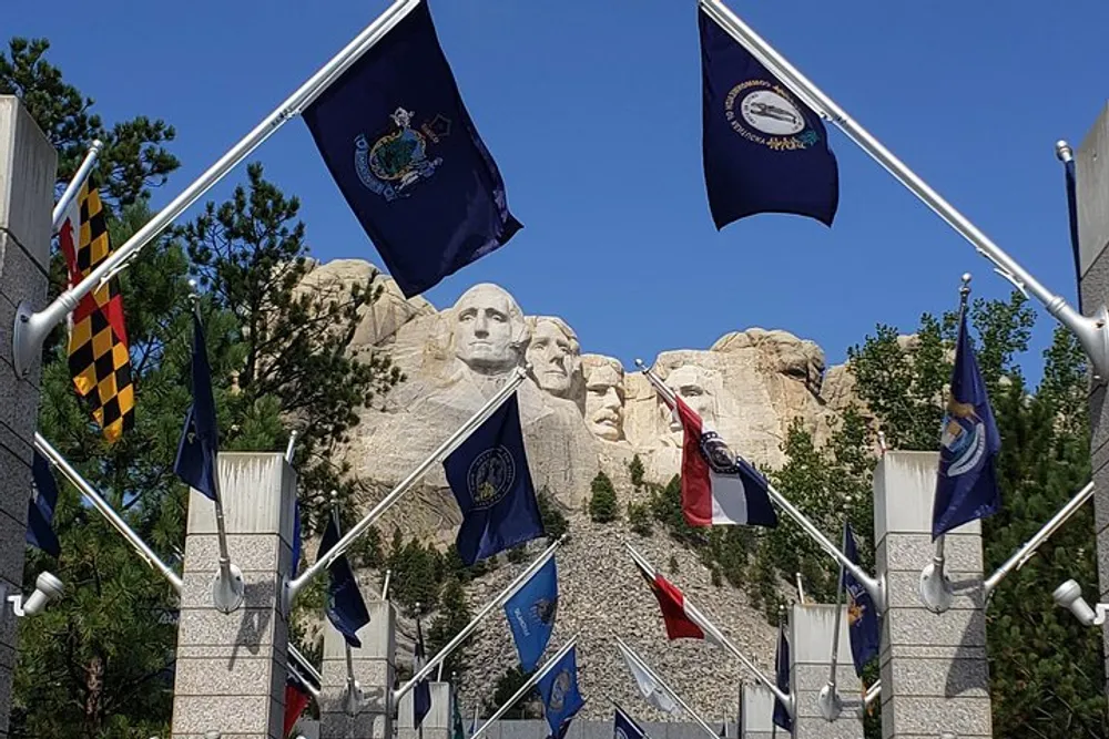 The image shows the iconic Mount Rushmore National Memorial framed by a display of various US state flags