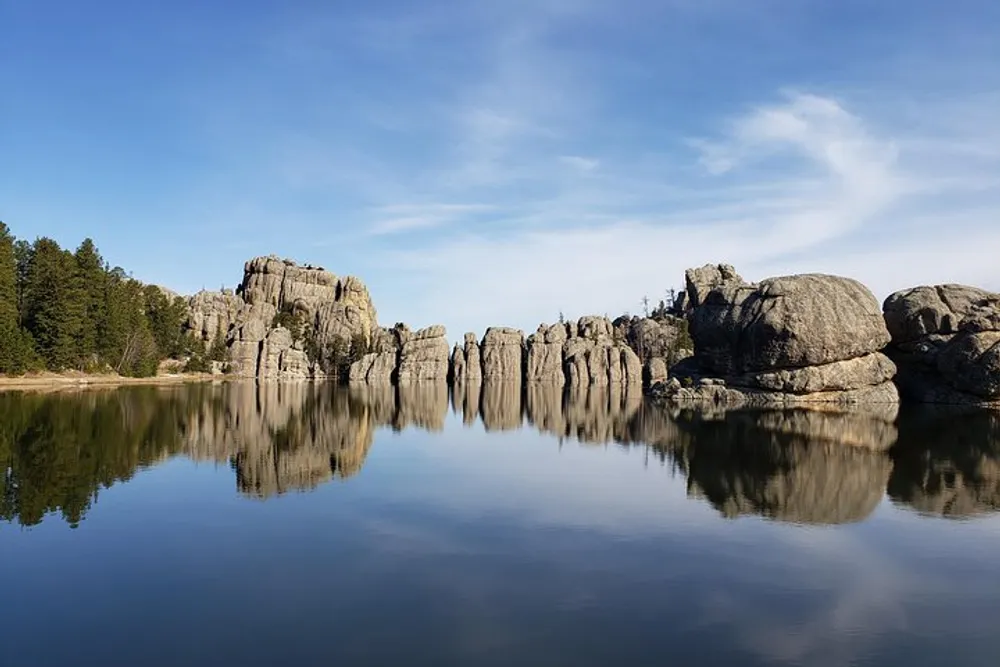 The image shows a tranquil lake reflecting towering rock formations and trees under a clear blue sky
