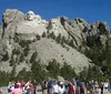 This image shows a crowd of visitors gazing at the iconic Mount Rushmore National Memorial under a clear blue sky