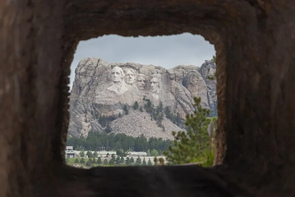 This image captures a view of Mount Rushmore National Memorial through a tunnel-like opening framing the famous sculptures of four US presidents