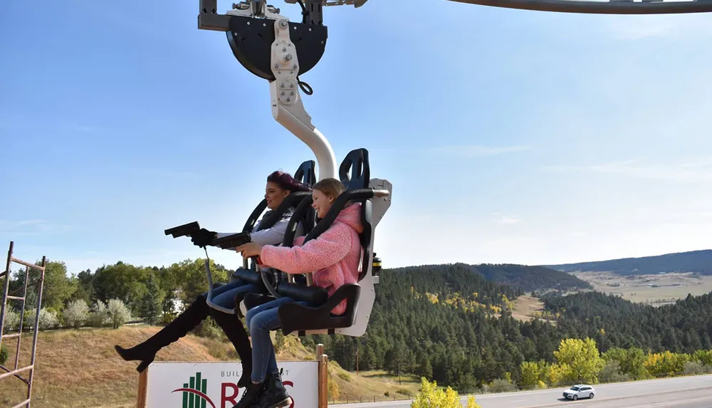 Two individuals are seated on an outdoor amusement ride that simulates a hang-gliding experience