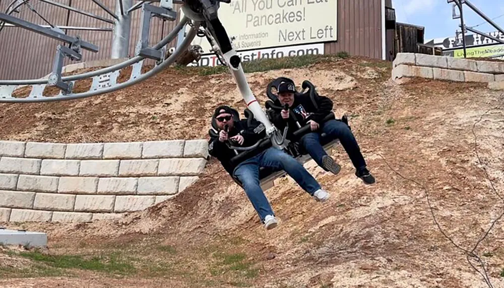 Two people are enjoying a ride on a mountain coaster giving thumbs-up as they descend along the track