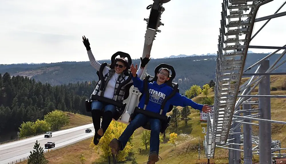Two people are joyfully experiencing a thrilling amusement park ride with a scenic backdrop