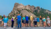 Tourists are gathered at an observation area to view the Mount Rushmore National Memorial, which features the carved faces of four U.S. presidents.