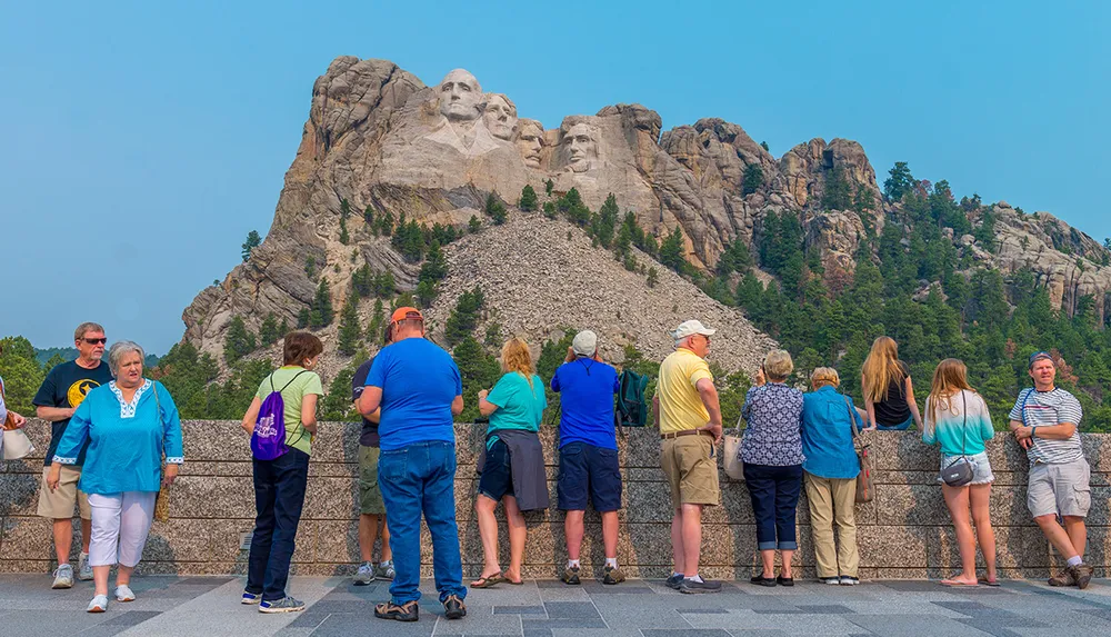 Tourists are gathered at an observation area to view the Mount Rushmore National Memorial which features the carved faces of four US presidents