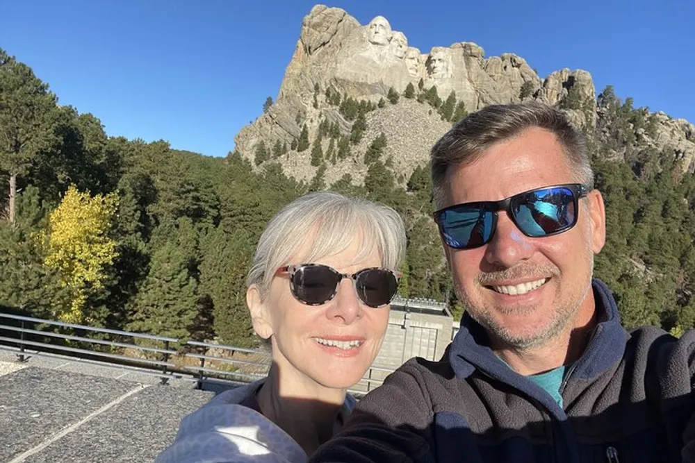 A smiling man and woman take a selfie with Mount Rushmore in the background