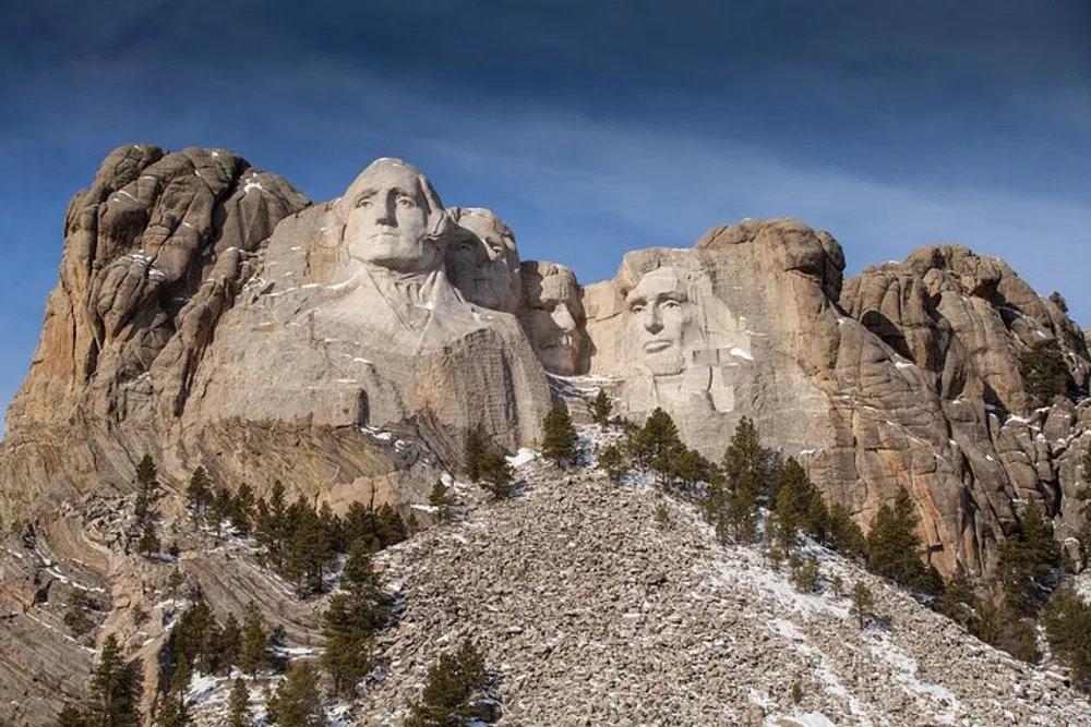 The image captures the grandeur of Mount Rushmore National Memorial showing the colossal carved faces of four former US presidents against a blue sky with spotty clouds