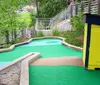 A person wearing black high-top sneakers is playing miniature golf on a green course with a red putter preparing to hit a blue ball