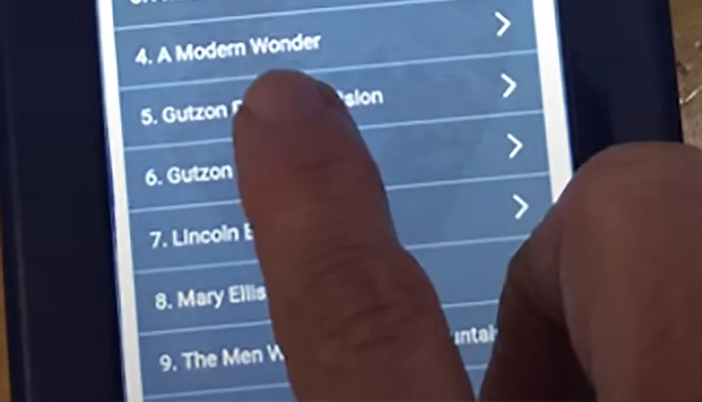 A person is using their finger to scroll through a list on a digital tablet which includes items named A Modern Wonder and Gutzon Borglum among others