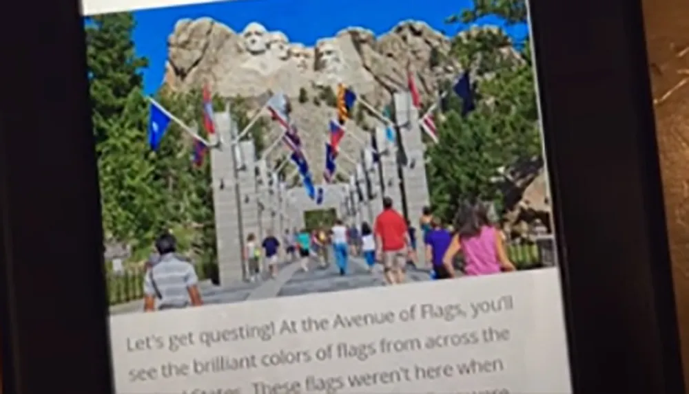 This image depicts visitors walking down the Avenue of Flags with a view of Mount Rushmore in the background