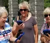 Three smiling women are using audio guide devices likely on an outdoor tour