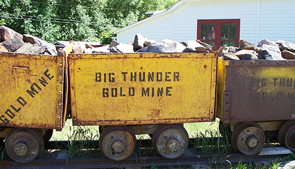 Two old weathered mining carts labeled BIG THUNDER GOLD MINE are filled with rocks and parked on tracks