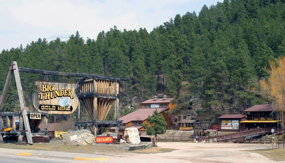The image shows the entrance to the Big Thunder Gold Mine with a rustic wooden sign set against a backdrop of pine-covered hills