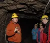 A group of people wearing hard hats listens to a man gesturing while giving a tour inside a cave or mine