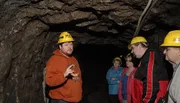 A group of people wearing hard hats listens to a man gesturing while giving a tour inside a cave or mine.