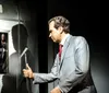 A wax figure resembling a historical figure is seated at a desk with an American flag to the right and blue curtains in the background