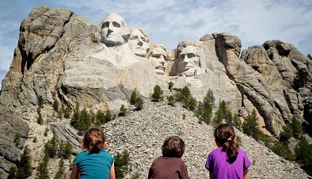 Three children are gazing at the monumental sculpture of four US presidents carved into Mount Rushmore