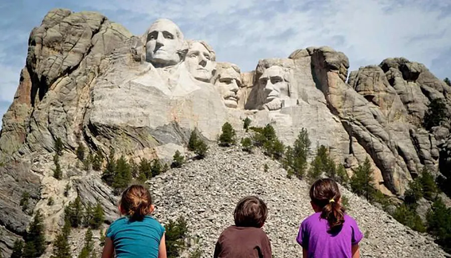 Three children are gazing at the monumental sculpture of four U.S. presidents carved into Mount Rushmore.