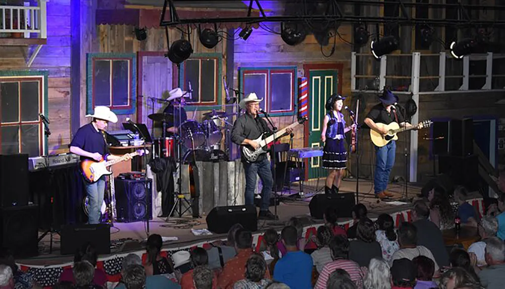 A band performs on stage in front of an audience in a venue decorated with rustic wooden facades