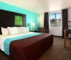 This image shows a neatly arranged hotel room with a colorful accent wall featuring a large bed a sitting area a mounted artwork and modern lamps