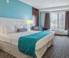 The image depicts a neatly arranged hotel room with a large bed vibrant accent wall and contemporary furnishings