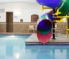 An indoor swimming pool with a colorful slide and a play area displaying safety signs and depth indicators on the walls