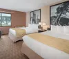 The image shows a neatly organized hotel room with two beds a window with a forest view and large black and white photos as decor