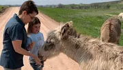 Two people are interacting with a donkey on a dirt road, with one of them offering it a carrot.