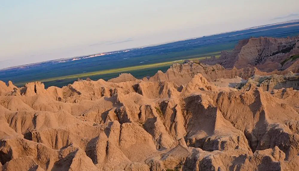 The image showcases a rugged landscape with sharp pinnacles and eroded rock formations bathed in the warm glow of what appears to be sunset lighting