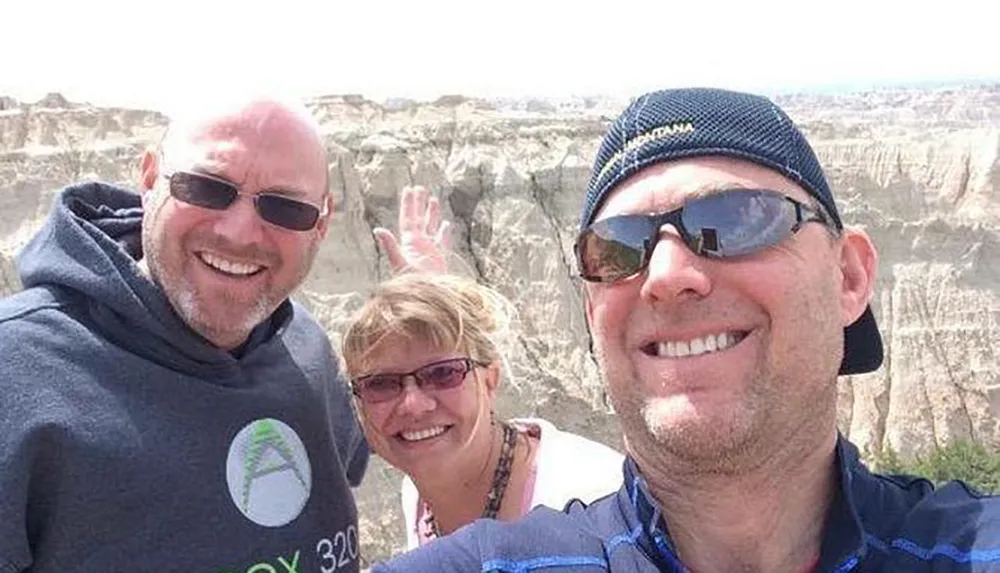 Three people are smiling for a selfie with a rocky canyon landscape in the background