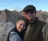 A couple is posing for a photo with a backdrop of rugged eroded rock formations under a bright sky