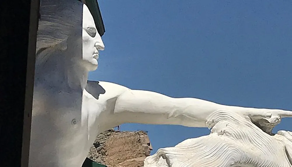 The image shows a large white statue of a human figure pointing outward set against a clear blue sky