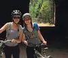 Two people are enjoying a bike ride along a gravel path lined with a wooden fence amidst green trees