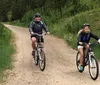 Two people are enjoying a bike ride along a gravel path lined with a wooden fence amidst green trees