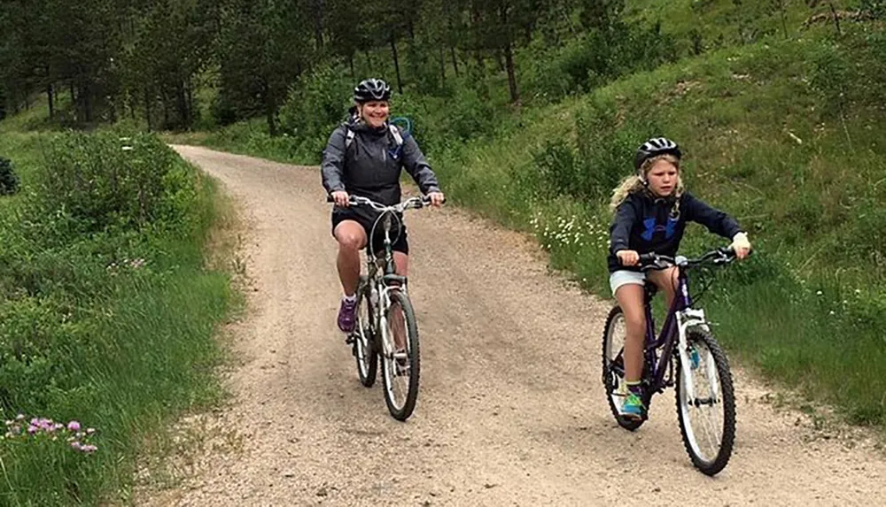 Two people are enjoying a bike ride on a dirt path through a green wooded area