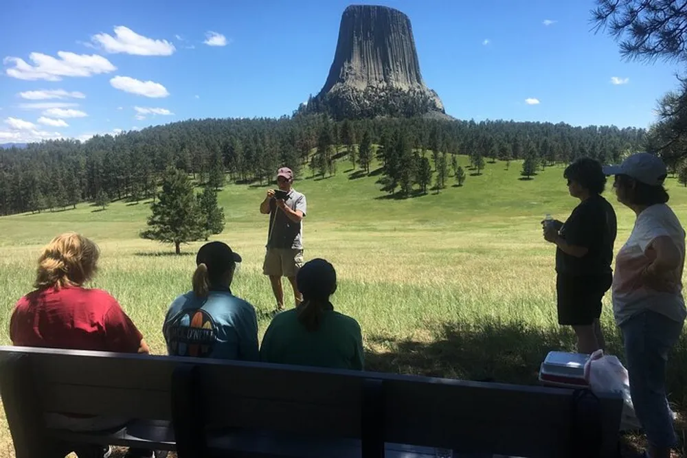 A group of people is listening to a speaker in front of the impressive Devils Tower natural monument