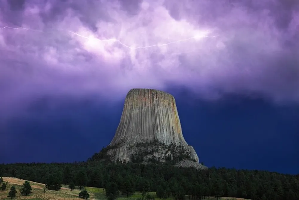 A striking butte rises prominently against a dramatic sky illuminated by lightning