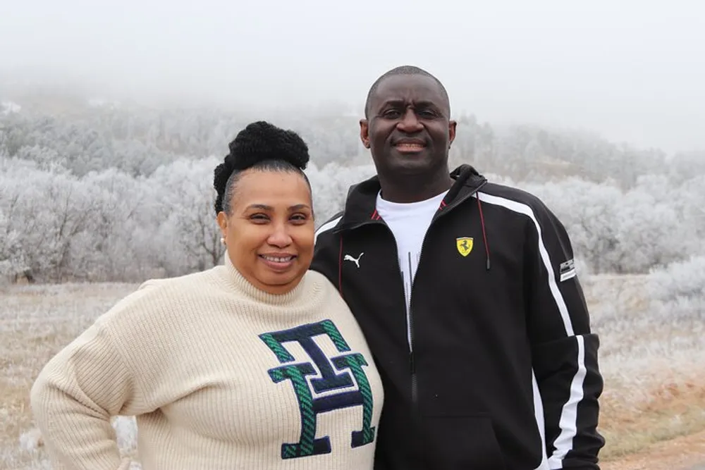 A man and a woman are smiling for the camera with a frosty landscape in the background