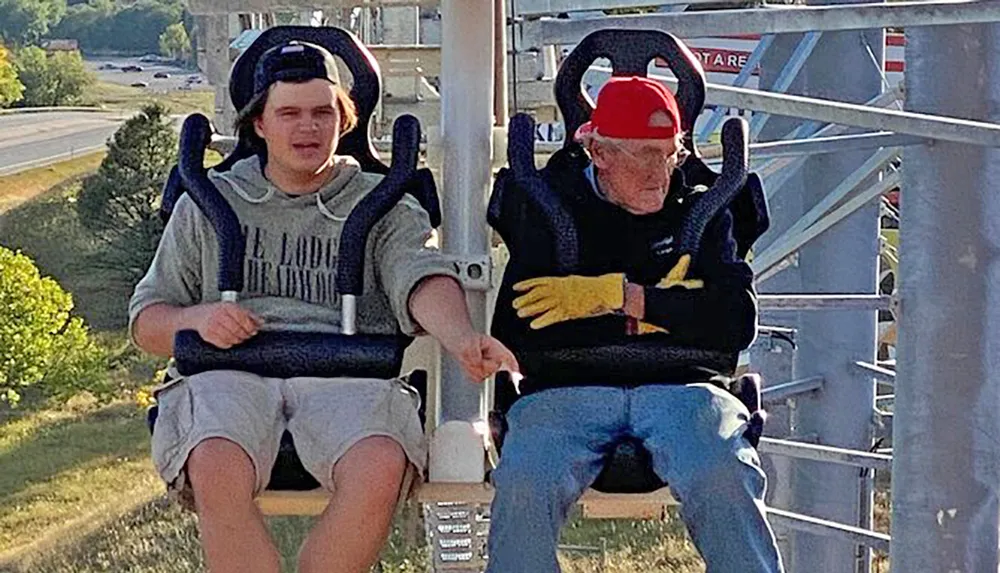 Two people are seated on an amusement park ride with over-the-shoulder restraints appearing ready for an exciting experience