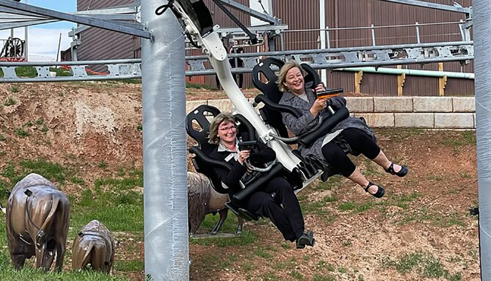 Two people are laughing and enjoying a ride on an amusement park attraction with metal sculptures of buffalo in the foreground