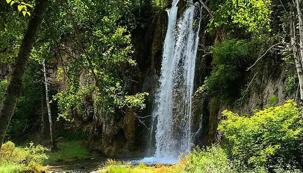 The image shows a serene waterfall cascading down a rocky cliff into a lush green landscape